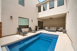 Une piscine avec des chaises longues, un canapé et un ventilateur de plafond, le tout dans une maison moderne.