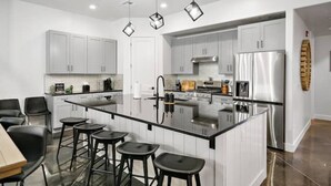 A modern kitchen with white cabinets, a central island with stools, stainless steel appliances, and pendant lighting. - The Sandlot - Sand Hollow & Zion - Entire Home with Private Pool (Hurricane)