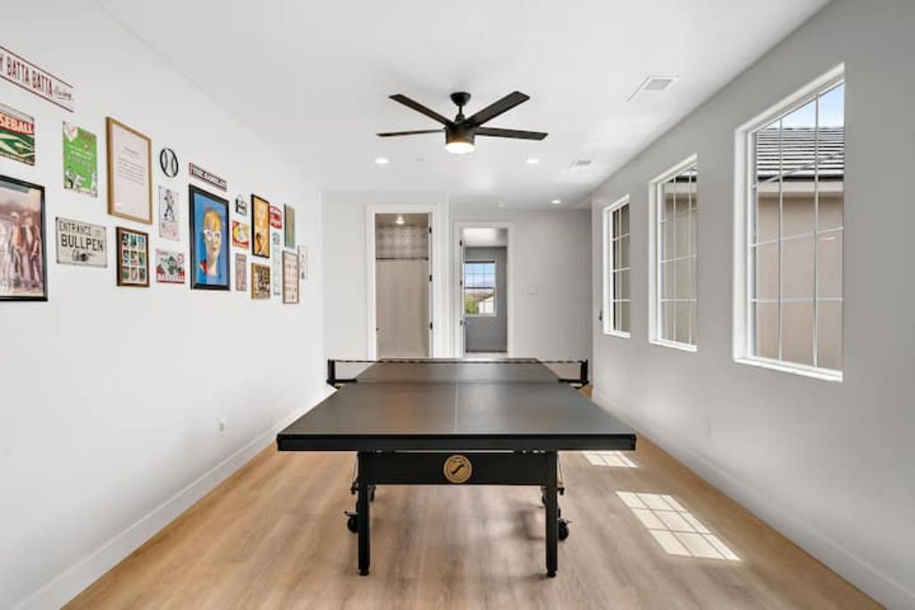 A room with a pool table, framed pictures on the wall, and large windows.