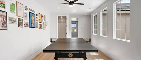 A room with a pool table, framed pictures on the wall, and large windows.