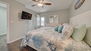 Ein Schlafzimmer mit Deckenventilator, einem Bett mit Blumenmuster-Überwurf, einem Fernseher an der Wand und einem Willkommensschild.