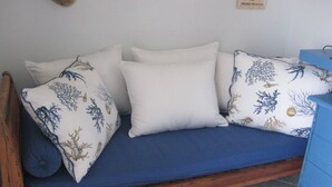 Un divano in legno con un cuscino blu, cuscini bianchi con motivi blu e dorati, e un comò blu con cassetti.