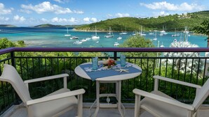 En balkon med et bord dækket til to, med udsigt over en lystbådehavn og en frodig grøn bakke i baggrunden.