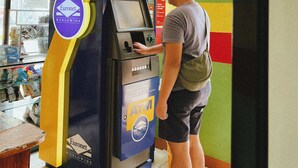 Un homme utilise un distributeur automatique de billets avec un panneau indiquant un service disponible 24 heures sur 24.