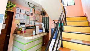 Un espace d’accueil d’hôtel comprenant un comptoir, un escalier et un mur décoré de certificats et de plantes.
