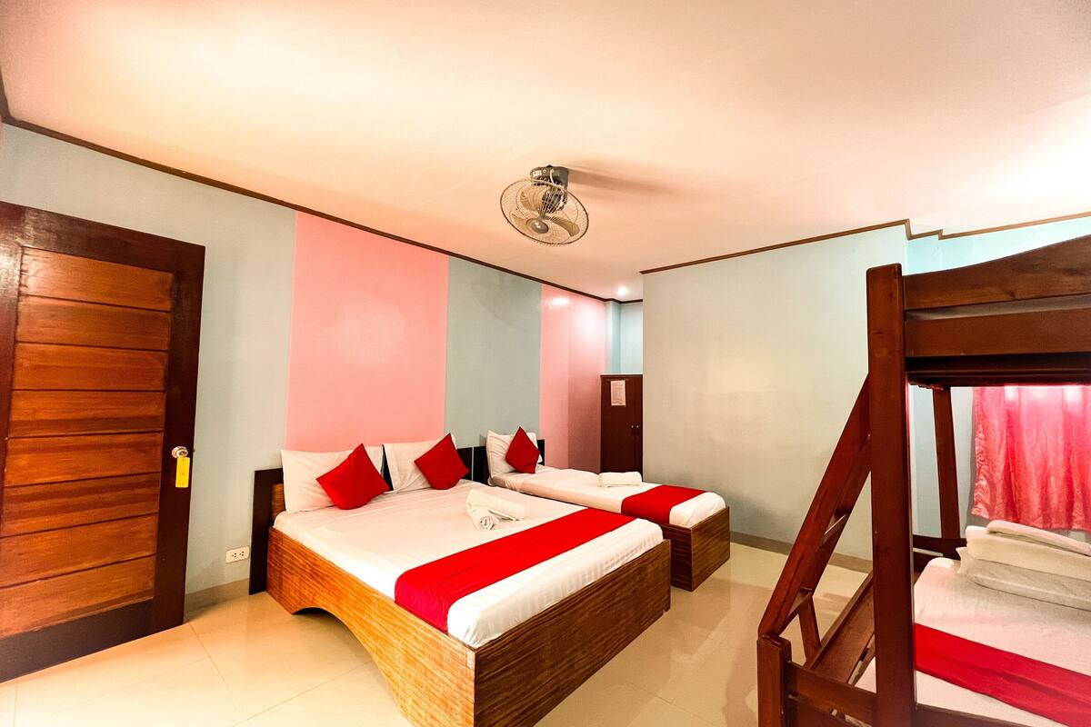 Ein Hotelzimmer mit einem hölzernen Bett, einem Etagenbett, einem Deckenventilator und einer Tür.