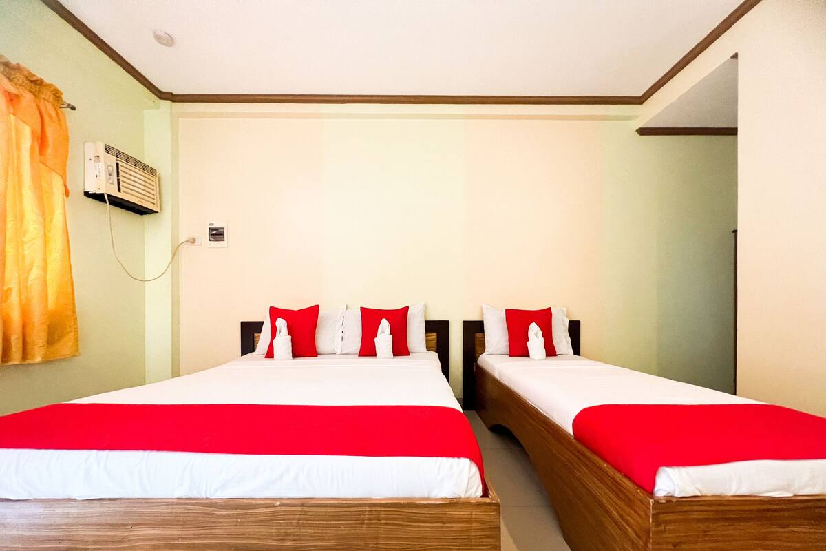 Ein Hotelzimmer mit zwei Betten, jeweils mit rot-weiß gestreifter Bettwäsche, einer Wand-Klimaanlage und einem Vorhang auf der linken Seite.