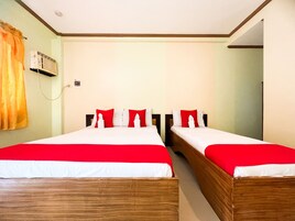 Habitación de hotel con dos camas, cada una con ropa de cama roja y blanca, un aire acondicionado de pared y una cortina a la izquierda.
