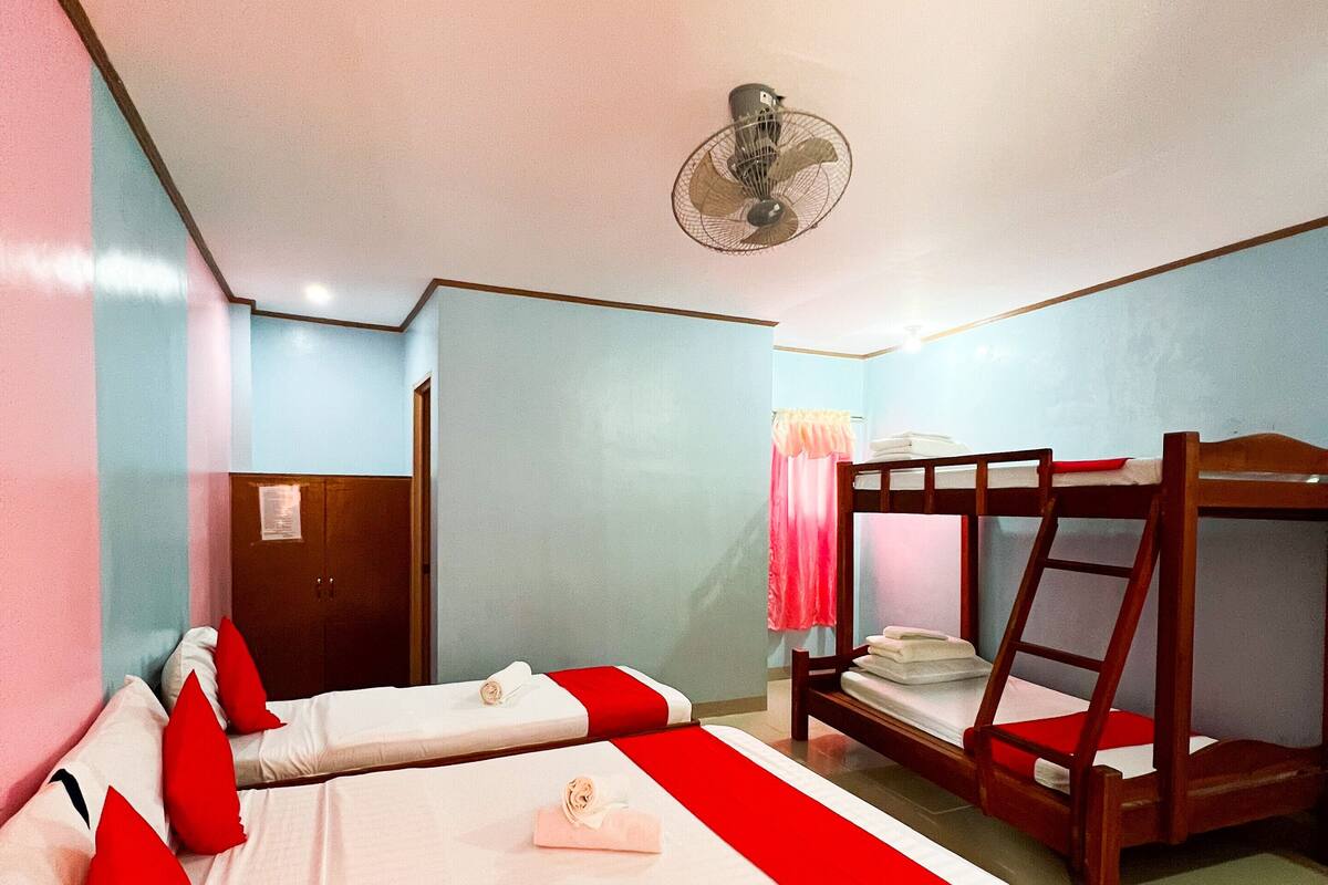 Ein Hotelzimmer mit zwei Betten, einem Schlafsofa und einem Deckenventilator, sowie einer Tür mit Spiegel.