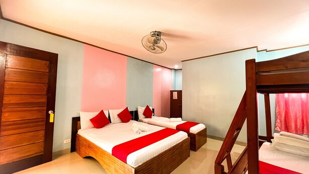 Une pièce avec deux lits en bois, un lit superposé, un ventilateur de plafond et une porte.