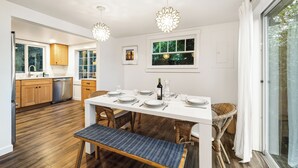 Una cocina moderna con armarios de madera, una encimera blanca y una zona de comedor con una mesa blanca dispuesta para cuatro personas.