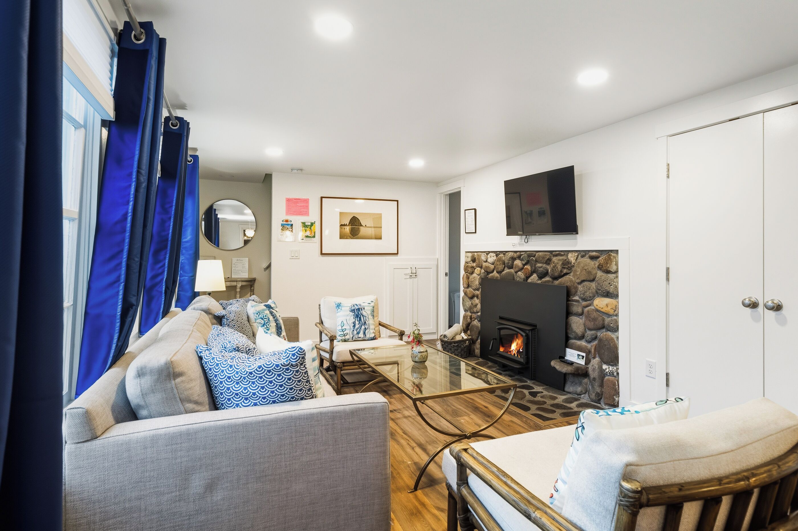 A living room with a glass coffee table, a sofa, a chair, a fireplace, and a TV mounted on the wall.