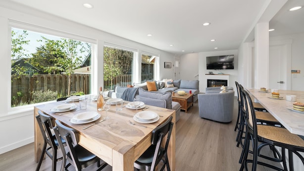 A modern kitchen with a dining area, large windows, and a flat-screen TV.