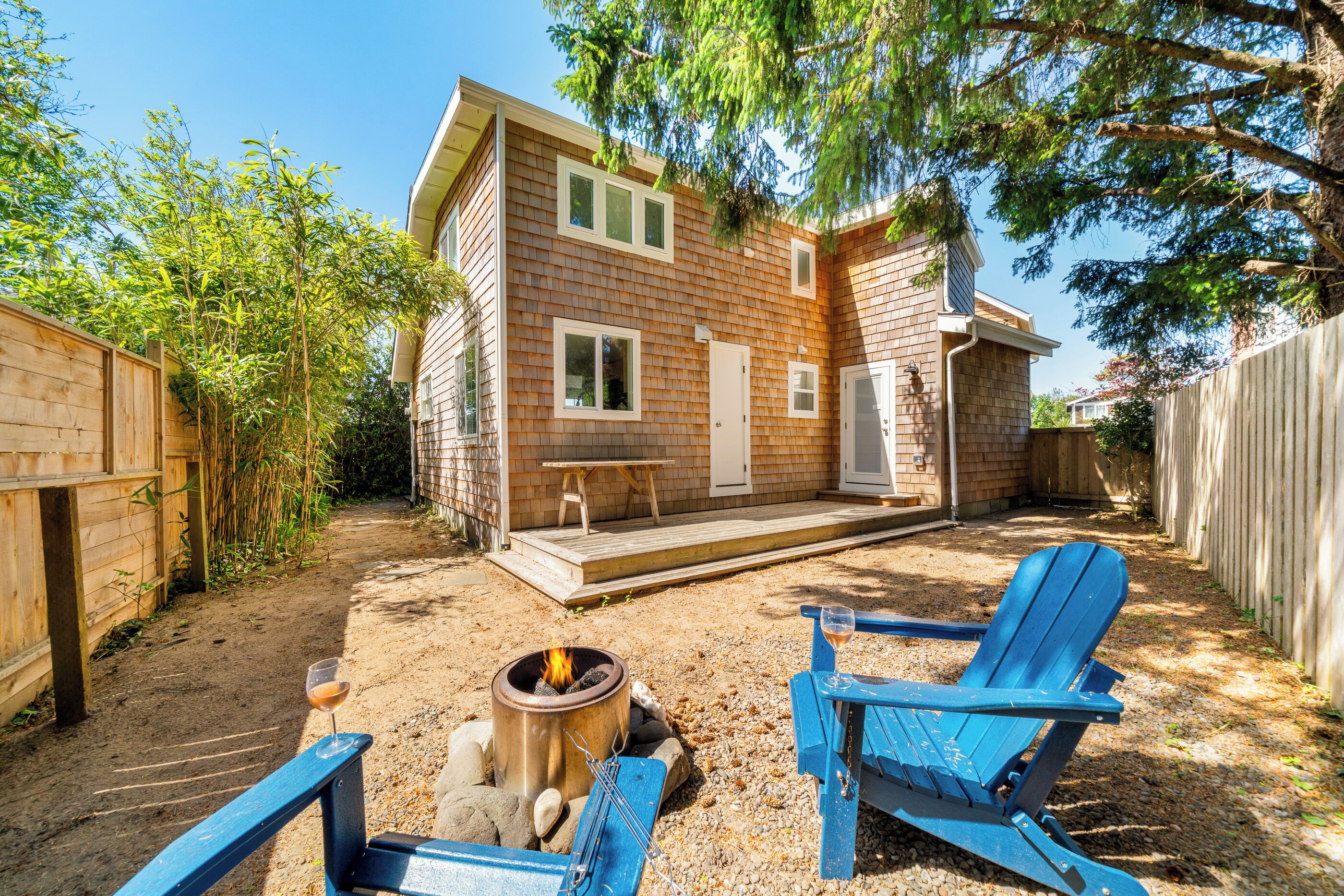A wooden house with a deck, a fire pit, and two blue Adirondack chairs.