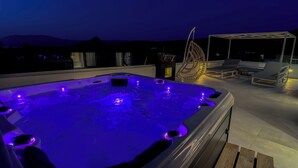 Un jacuzzi con iluminación azul en una terraza en la azotea, con sillones de descanso y vistas a las montañas.