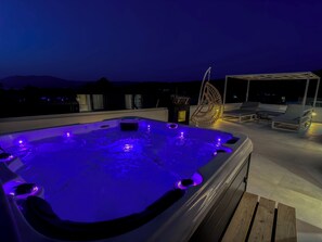 Een jacuzzi met blauwe verlichting op een dak terras, met lounge stoelen en uitzicht op de bergen.