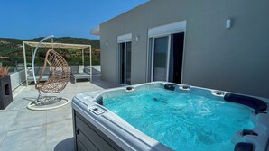 Terraza en la azotea con jacuzzi, una silla colgante y barandilla de vidrio con vistas a un paisaje montañoso.
