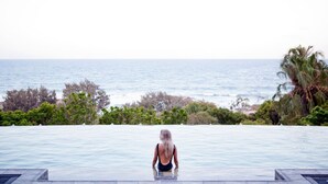 A person in a swimming pool with a view of the ocean and palm trees. - Finding Solace - Sunrise at 1770 (Agnes Water)