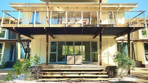 A two-story house with a balcony, large windows, and a covered front porch. - Drishti - Sunrise at 1770 (Agnes Water)