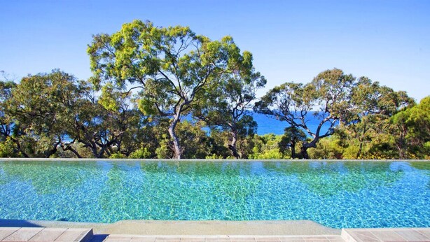 A clear swimming pool with a tiled deck in front, surrounded by trees and a clear sky. - Drishti - Sunrise at 1770 (Agnes Water)