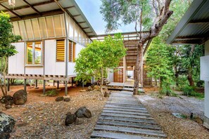 Uma casa moderna com um deck de madeira, área externa coberta e um jardim com pedras e árvores.