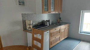 A compact kitchen with wooden cabinets, a built-in dishwasher, a coffee maker, and a window providing natural light.