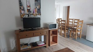 A compact living space with a wooden TV stand, a microwave, and a dining area with wooden chairs and a table.