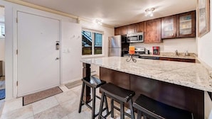 A kitchen with a marble countertop, stainless steel appliances, wooden cabinets, and a door. - Edelweiss Haus G | Hot Tub | Pool | Kitchen | Walk to Slopes (Park City)