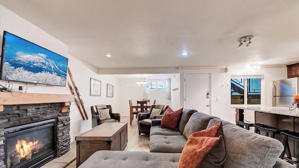 A living room with a fireplace, a sofa, a TV, and a dining area. - Edelweiss Haus G | Hot Tub | Pool | Kitchen | Walk to Slopes (Park City)