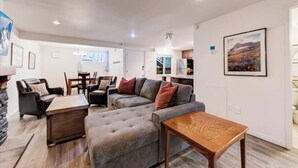 A modern living room with a grey sectional sofa, a wooden coffee table, and a dining area with a small table and chairs. - Edelweiss Haus G | Hot Tub | Pool | Kitchen | Walk to Slopes (Park City)