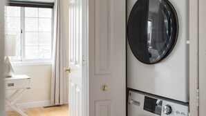 A laundry room with two stacked front-loading washing machines, a door leading to a room with a window and a desk. - Your Up North Getaway! (Traverse City)