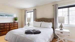 A neatly arranged bedroom with a bed, bedside tables, a dresser, and a window with curtains. - Your Up North Getaway! (Traverse City)