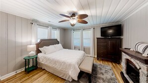 Une chambre à coucher avec un lit, un ventilateur de plafond, une télévision, une commode et une cheminée.
