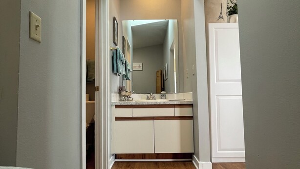 A narrow hallway with a bathroom featuring a sink, mirror, and towel rack. - Quiet & Cozy Pet-Friendly Condo with Pool & Garage  (Bettendorf)