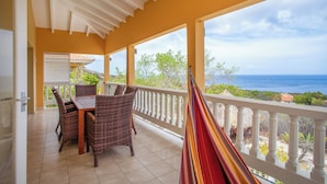 A covered patio with a dining table and chairs, a hammock, and a view of the ocean. - Holiday Home Gran Veranda with private pool and ocean view, Coral Estate (Willemstad, Curacao, Curacao, Caribbean)
