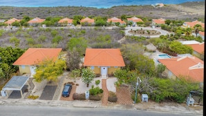 A coastal residential area with houses having red-tiled roofs, a clear view of the ocean, and a paved road in the foreground. - Holiday Home Gran Veranda with private pool and ocean view, Coral Estate (Willemstad, Curacao, Curacao, Caribbean)