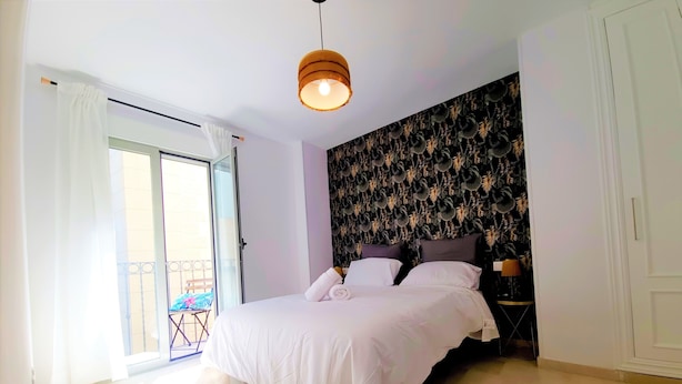 Een slaapkamer met een bed, een plafondlamp, een raam met gordijnen en een balkon.