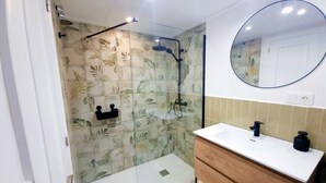 Een moderne badkamer met een douchecabine van glas, een houten wastafelmeubel en een spiegel boven de wastafel.