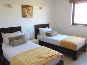 Two single beds with wooden headboards and white mattresses, each with matching bedding and pillows, are positioned in this cozy space.