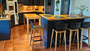 A modern kitchen with dark cabinets, a wooden island with bar stools, and a tiled floor. - Villa Marina , vue sur le Canal, à 5 Minutes du Centre Historique (Aigues-Mortes)