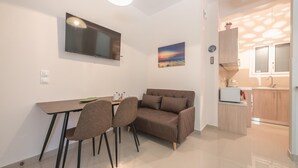 A compact living space with a dining area, a sofa, a TV, and a kitchenette. - Cozy Acropolis Studio by Cloudkeys (Athens)