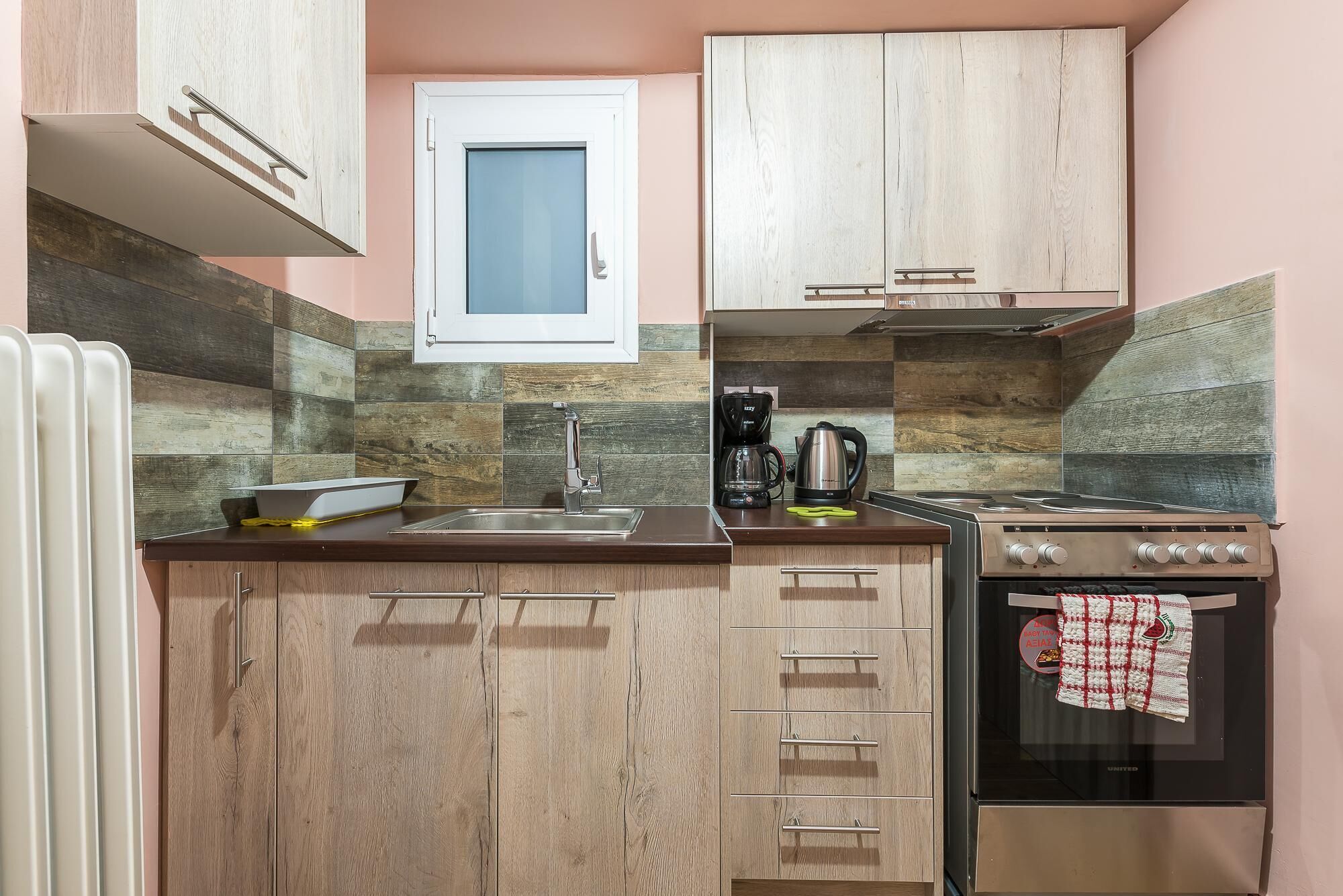 Cocina compacta con armarios de madera, horno integrado, cafetera y ventana sobre el lavadero.