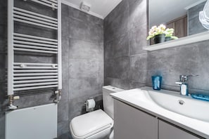 Ein modernes Badezimmer mit grauen Fliesen, einer weißen Toilette, einem weißen Waschbecken mit einem blauen Glas und einem Handtuchhalter.