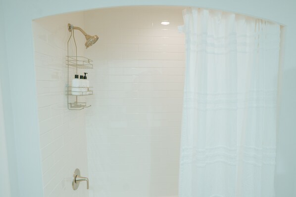 Un baño moderno con ducha, un estante de vidrio con artículos de aseo y una cortina blanca.