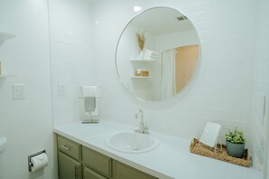 Un baño moderno con un lavamanos blanco, un espejo redondo y una pequeña planta en maceta.