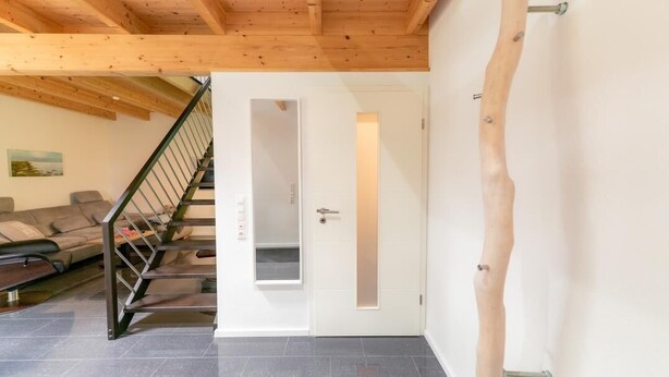 Ein modernes Interieur mit einer Treppe zu einer Tür mit der Aufschrift 'BULLA', einer Sofagarnitur und einer Holzzielung.
