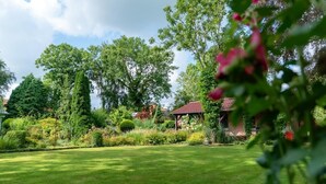 Ein gepflegter Garten mit Laube, verschiedenen Bäumen und einer Rasenfläche.