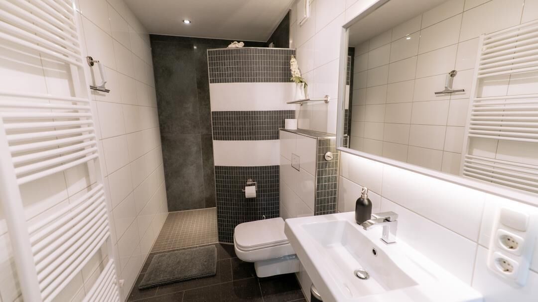 A modern bathroom with a white sink, a toilet, and a shower area with black and white tiles.