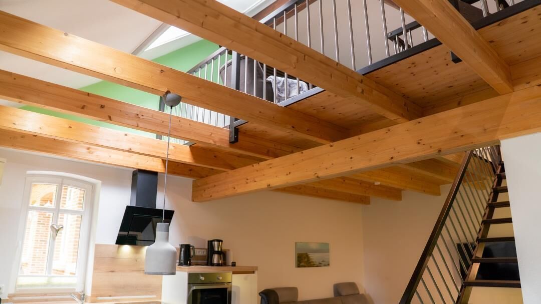 A spacious room with a high ceiling, wooden beams, a staircase, and a view of a balcony.