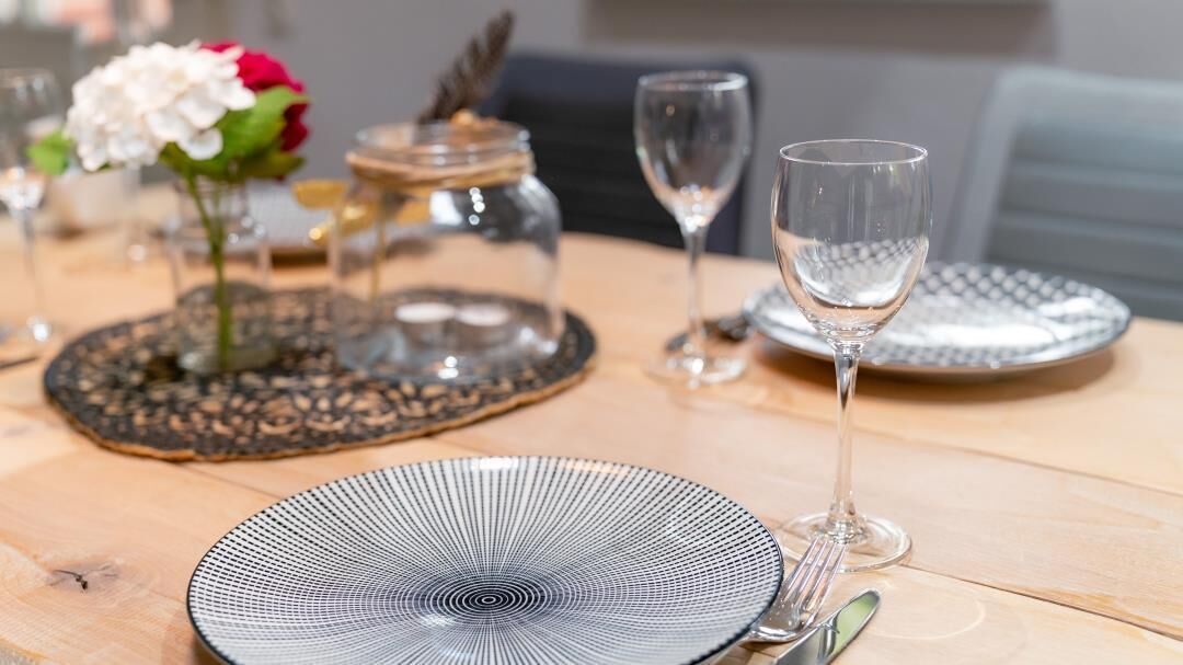A dining table set with a patterned plate, a clear glass, and a vase with flowers.